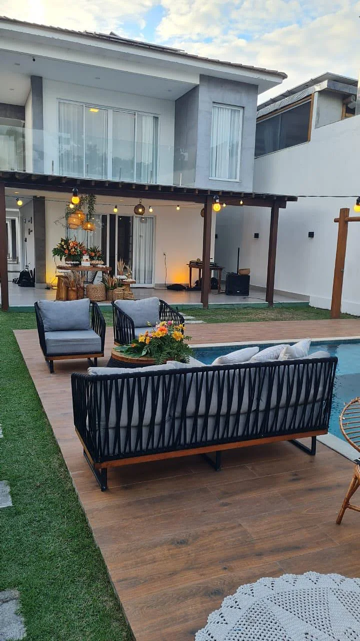 Sofá no deck de madeira, com a piscina e a casa ao fundo
