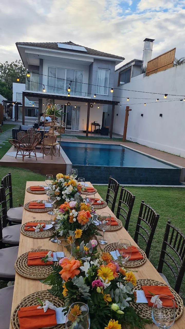 Mesa longa posta ao lado da piscina, com a casa ao fundo